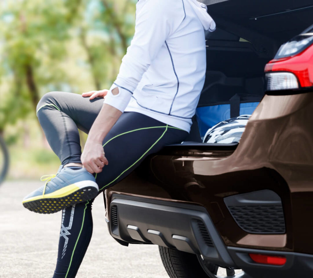 Femme ajustant ses souliers de jogging assise sur le bord du coffre du Mitsubishi RVR 2021